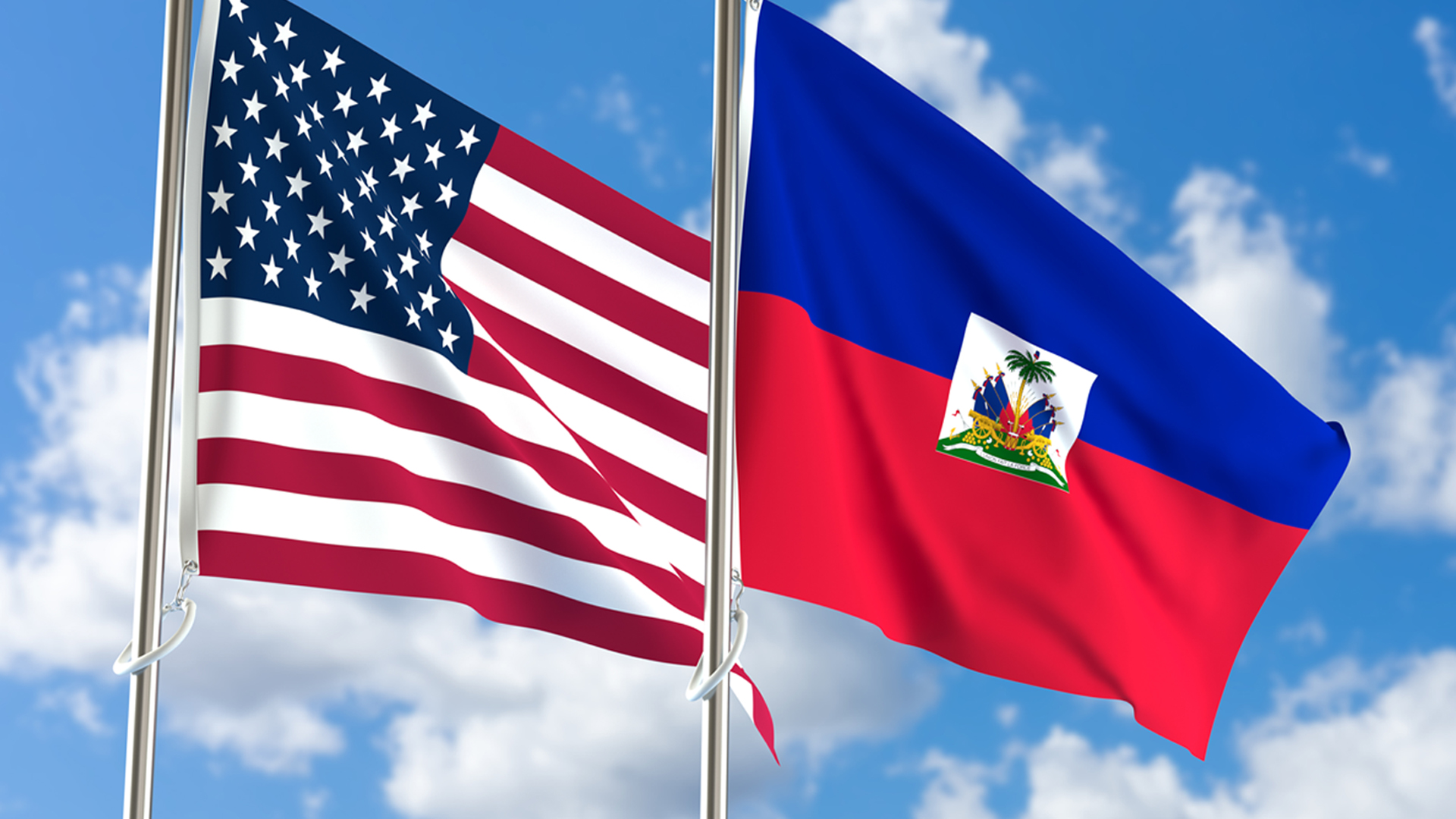 American and Haitian flags waving side by side under a blue sky, symbolizing unity and cultural pride.